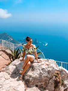 ragazza seduta in cima al Monte Solaro di Capri con i faraglioni sullo sfondo